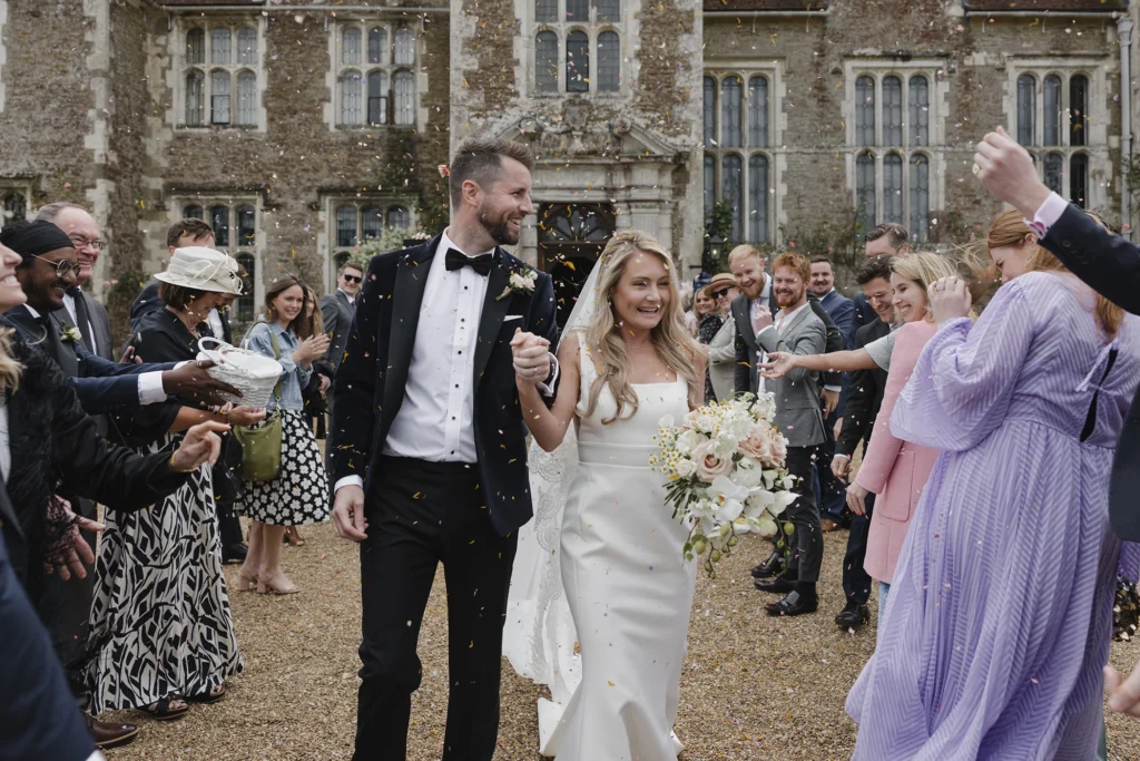 Bride and groom walking through confetti outside Loseley Park