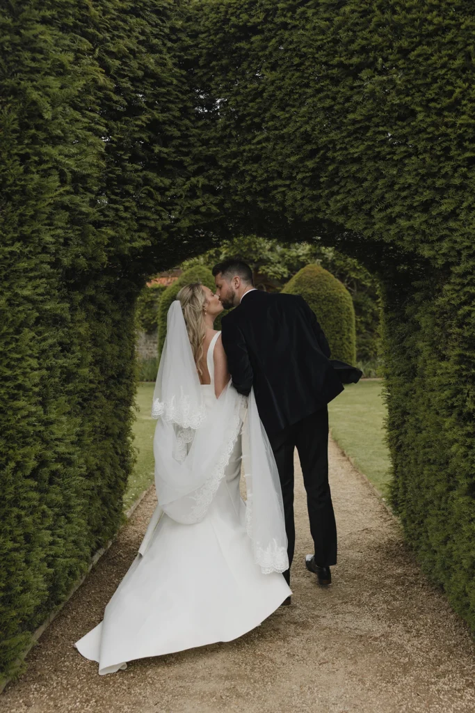 Bride and groom kissing under a green archway at Loseley Park.