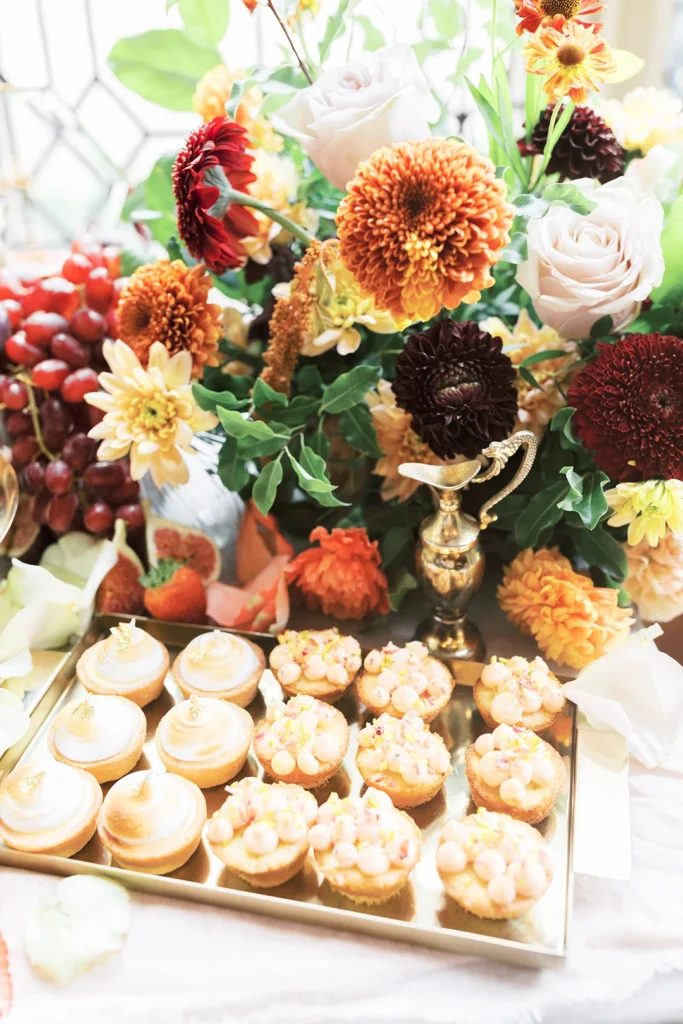 Assortment of delicate wedding pastries surrounded by colorful floral arrangements.