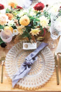 Elegant wedding table setting featuring glass plates, golden cutlery, and floral centerpiece.