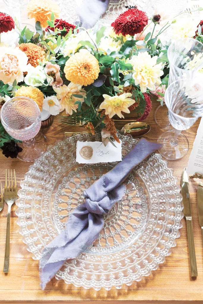 Elegant wedding table setting featuring glass plates, golden cutlery, and floral centerpiece.