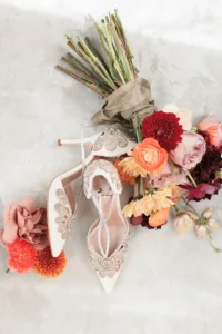 Bridal shoes with intricate embellishments paired with a colorful floral bouquet.