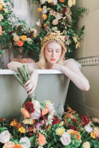 Bride in a floral crown surrounded by vibrant flowers in an elegant bathtub setting.