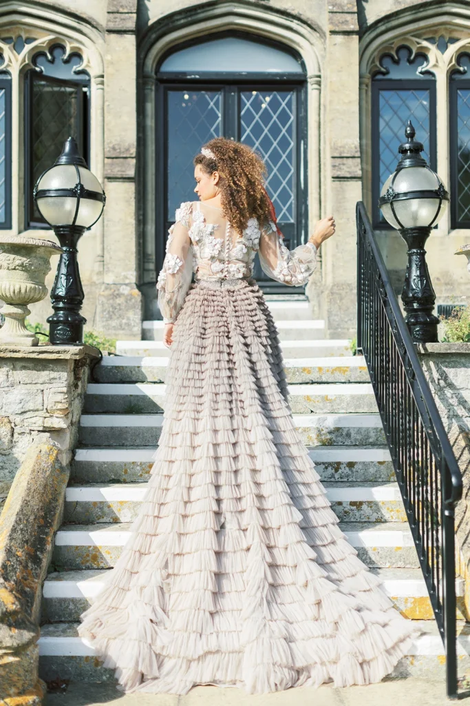 Bride wearing a ruffled gown ascending Nutfield Priory’s grand staircase.