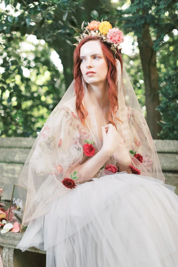 Elegant red-haired bride in a floral veil and crown, seated outdoors at Nutfield Priory.