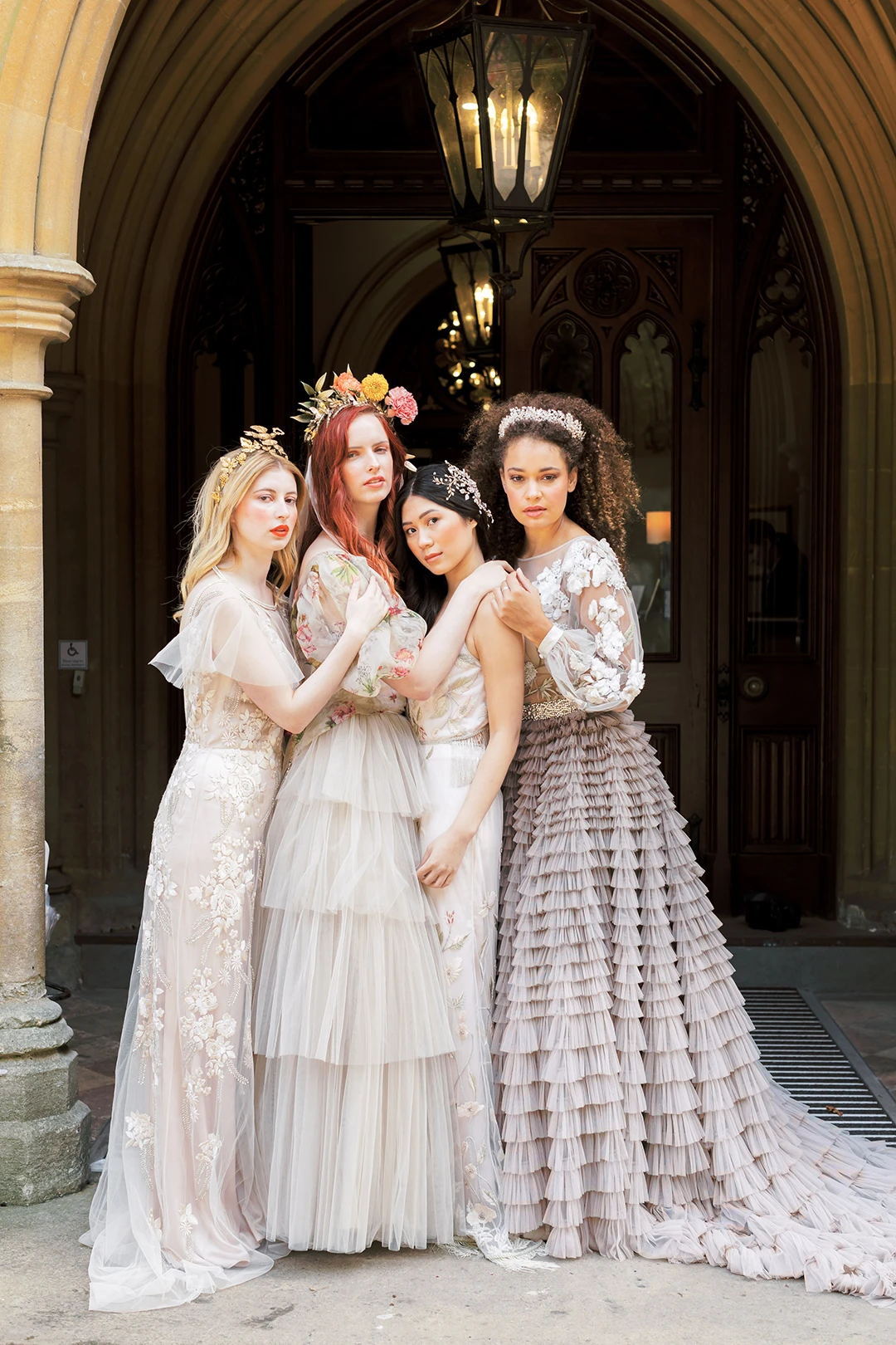 Brides in intricate gowns standing together under the elegant entrance of Nutfield Priory.