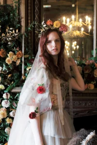 Bride with a floral veil standing by a luxurious mirror and floral arrangements at Nutfield Priory.