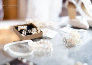 Bridal accessories including pearl earrings and floral details on a reflective table during a Pelham House photoshoot.