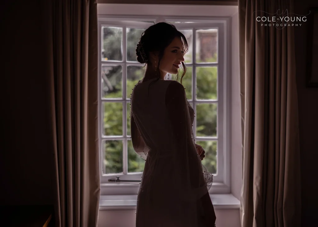 Bride standing near a window in soft lighting during Pelham House photoshoot.