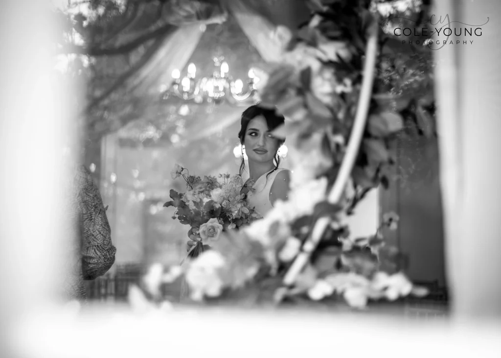 Bride reflected through a floral arch, holding her bouquet at Pelham House.