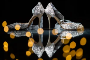 Ornate bridal heels adorned with pearls and flowers against a reflective surface with golden bokeh, part of Pelham House wedding photoshoot.