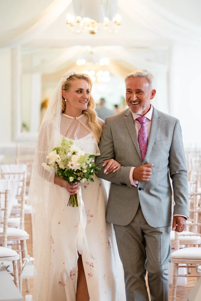 Smiling bride walking down the aisle with her father at Pelham House wedding.