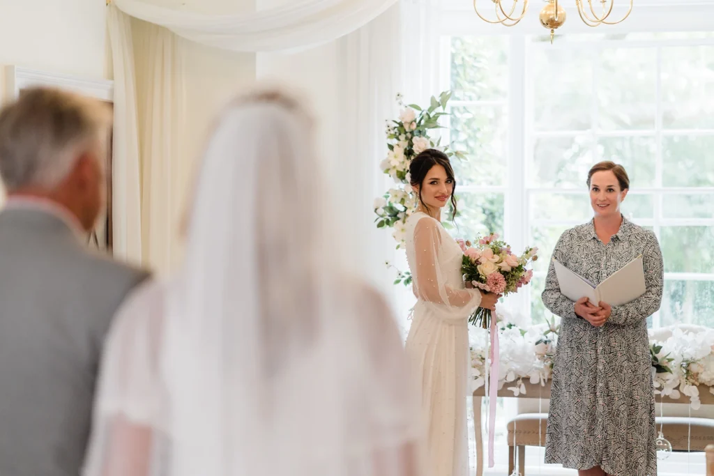 Bride holding her bouquet during the ceremony at Pelham House, with an elegant floral backdrop.