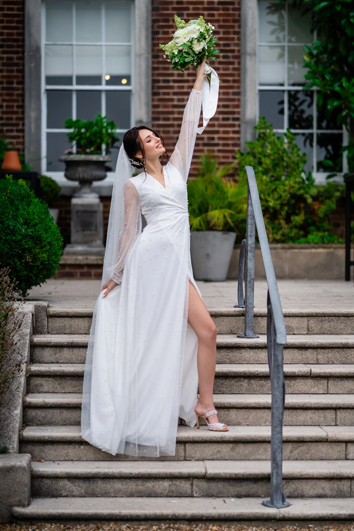 Bride holding a bouquet aloft on the steps of Pelham House during the photoshoot.