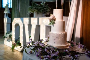 Wedding cake with floral accents in front of illuminated "LOVE" letters at Pelham House.