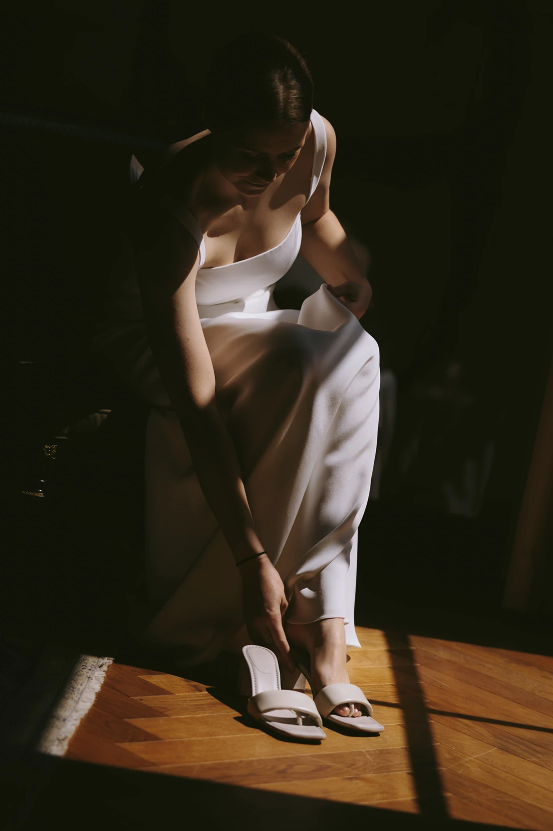 Bride adjusting her minimalist satin wedding dress in soft lighting.