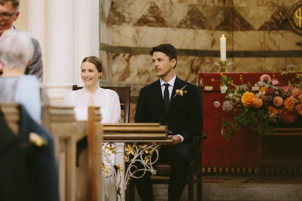 Bride and groom sitting during their wedding ceremony in a London church, showcasing minimalist elegance.