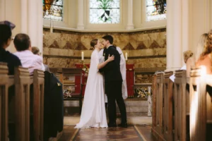 The bride and groom share a kiss at the altar in a London church, embracing a minimalist wedding style.