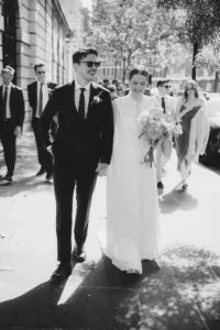 Bride and groom walking hand-in-hand on a sunny street after their minimalist London wedding.