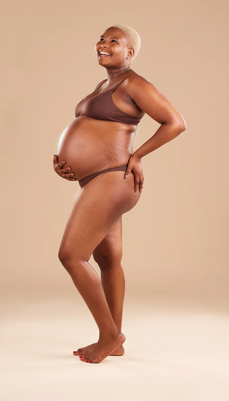 Smiling pregnant woman posing in brown lingerie.