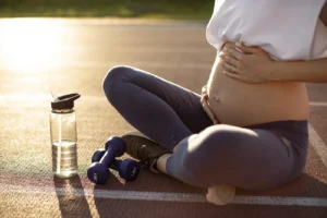 Pregnant woman sitting outdoors with water bottle and dumbbells