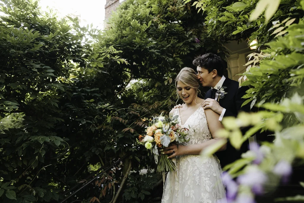 Bride and groom posing outdoors surrounded by greenery