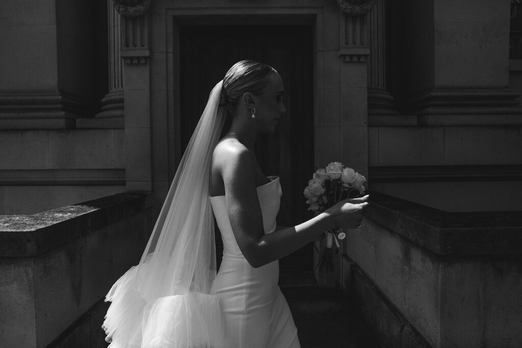 Black and white profile of a bride holding her bouquet in an elegant city setting