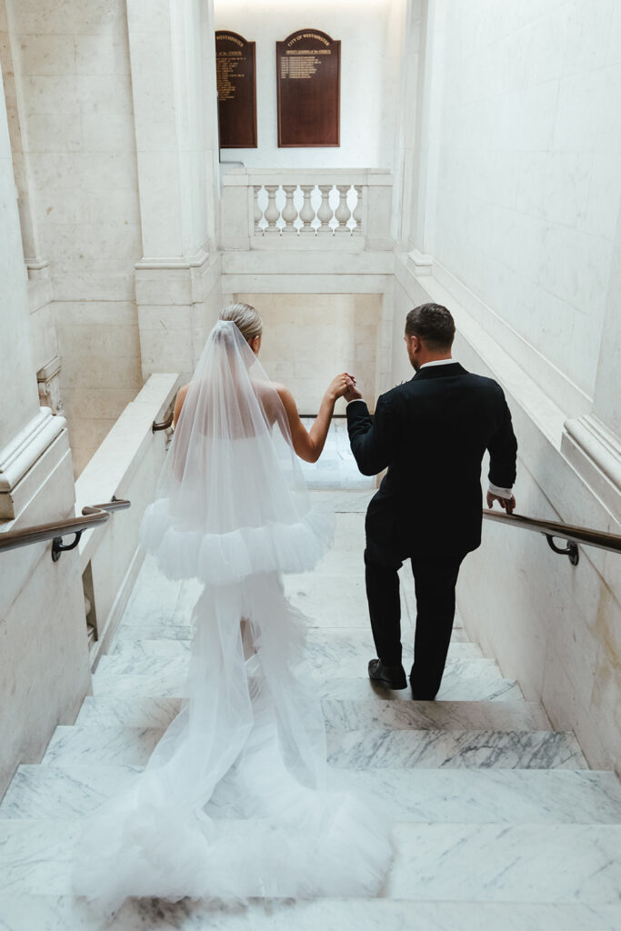 Newlyweds walking hand in hand down a marble staircase in a grand wedding venue