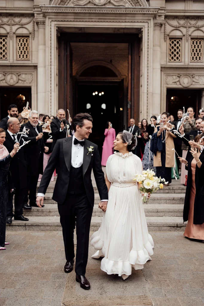 Elegant wedding couple walking hand in hand through cheering guests