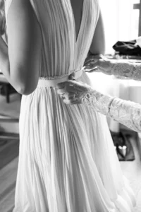 Hands adjusting the waistband of the bride’s beautifully pleated wedding gown with pearl embellishments before the elegant wedding ceremony