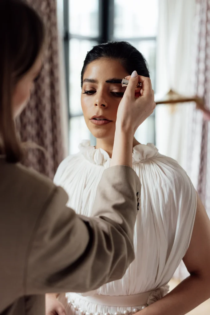 Bride getting a final makeup touch-up with her makeup artist perfecting her brows for a flawless, elegant wedding look