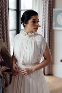 Bride standing in a softly lit room, adjusting her wedding gown, exuding elegance and grace before her elegant wedding