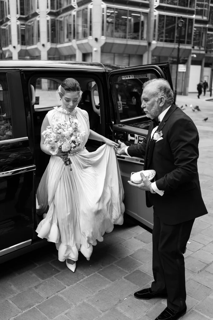 Bride stepping out of a black car with father’s assistance