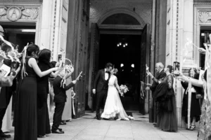 Newlyweds stepping out of the church as guests celebrate their elegant wedding