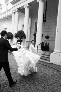 Groom lifting bride’s flowing gown as they walk together