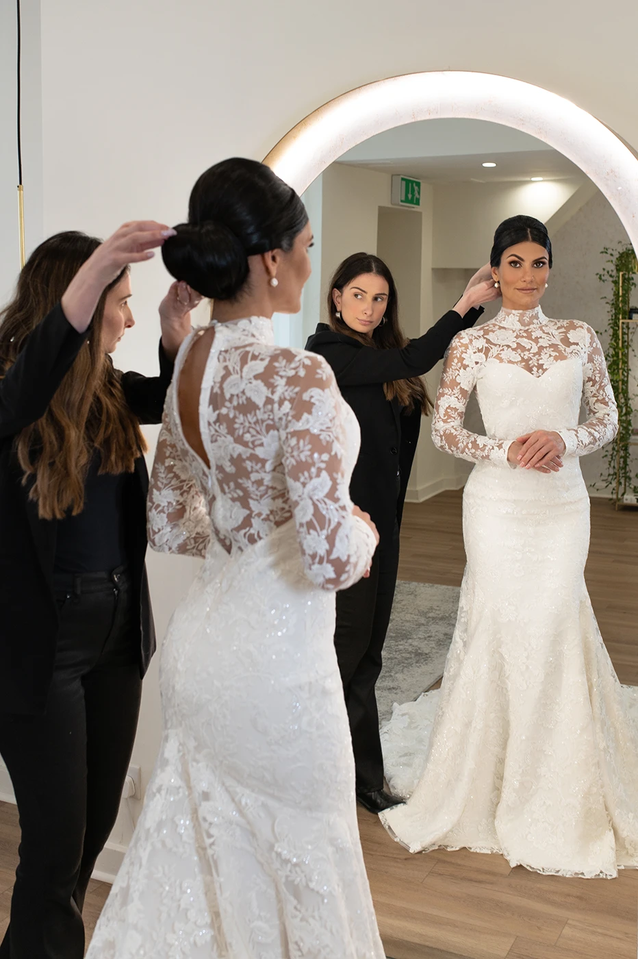 Makeup artist perfecting a bride’s sleek updo in front of a mirror