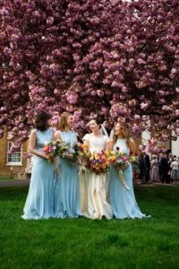 Bride with bridesmaids holding colourful bouquets under cherry blossoms