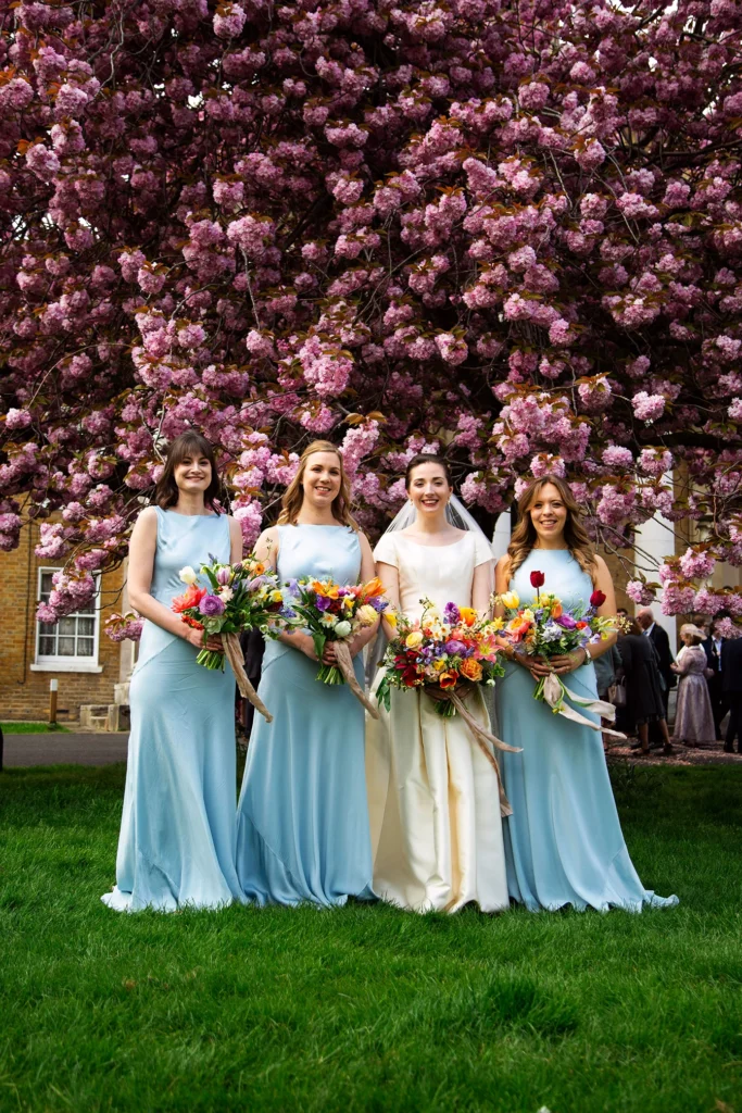 Bride and bridesmaids in pastel blue dresses under cherry blossoms at Asylum Chapel