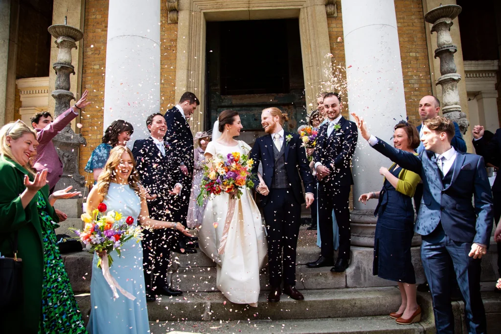 Bride and groom walking down Asylum Chapel steps as guests cheer and throw confetti