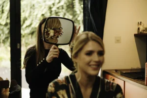 Bridal stylist showing the bride her elegant floral updo in a mirror before the wedding