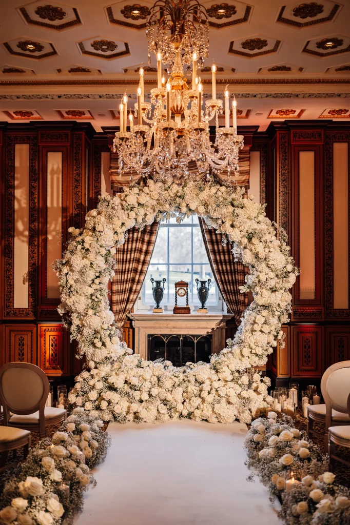 Luxurious indoor ceremony setup with a round white flower arch and chandelier
