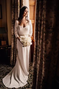 Bride in satin gown holding bouquet by the window at the Lanesborough