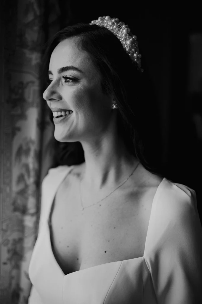 Bride smiling by the window, wearing pearl headband