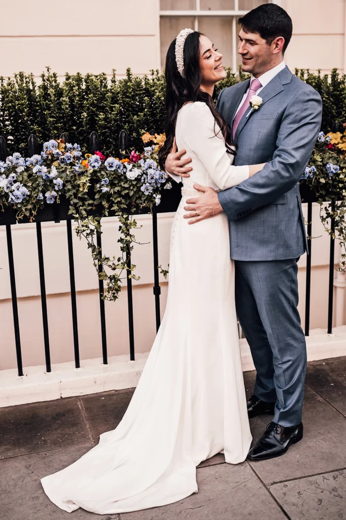 Bride and groom smiling and embracing in front of floral arrangement during wedding in Belgravia