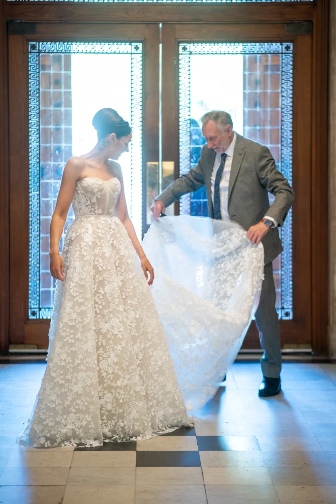 Bride in lace wedding dress being helped with her gown
