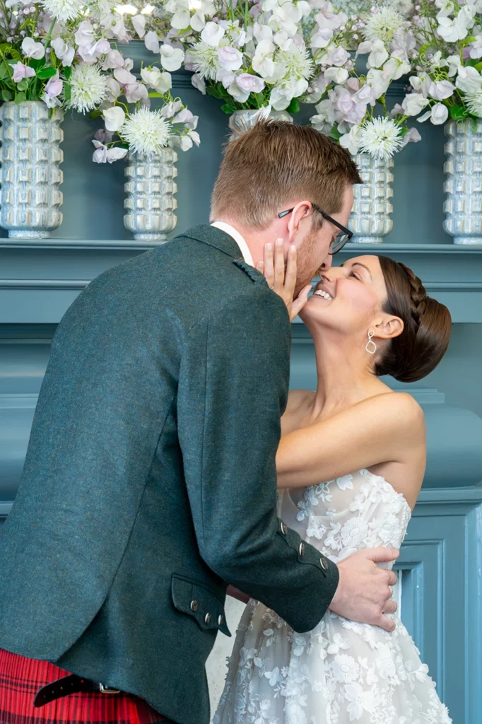 Bride and groom sharing a kiss in front of floral fireplace