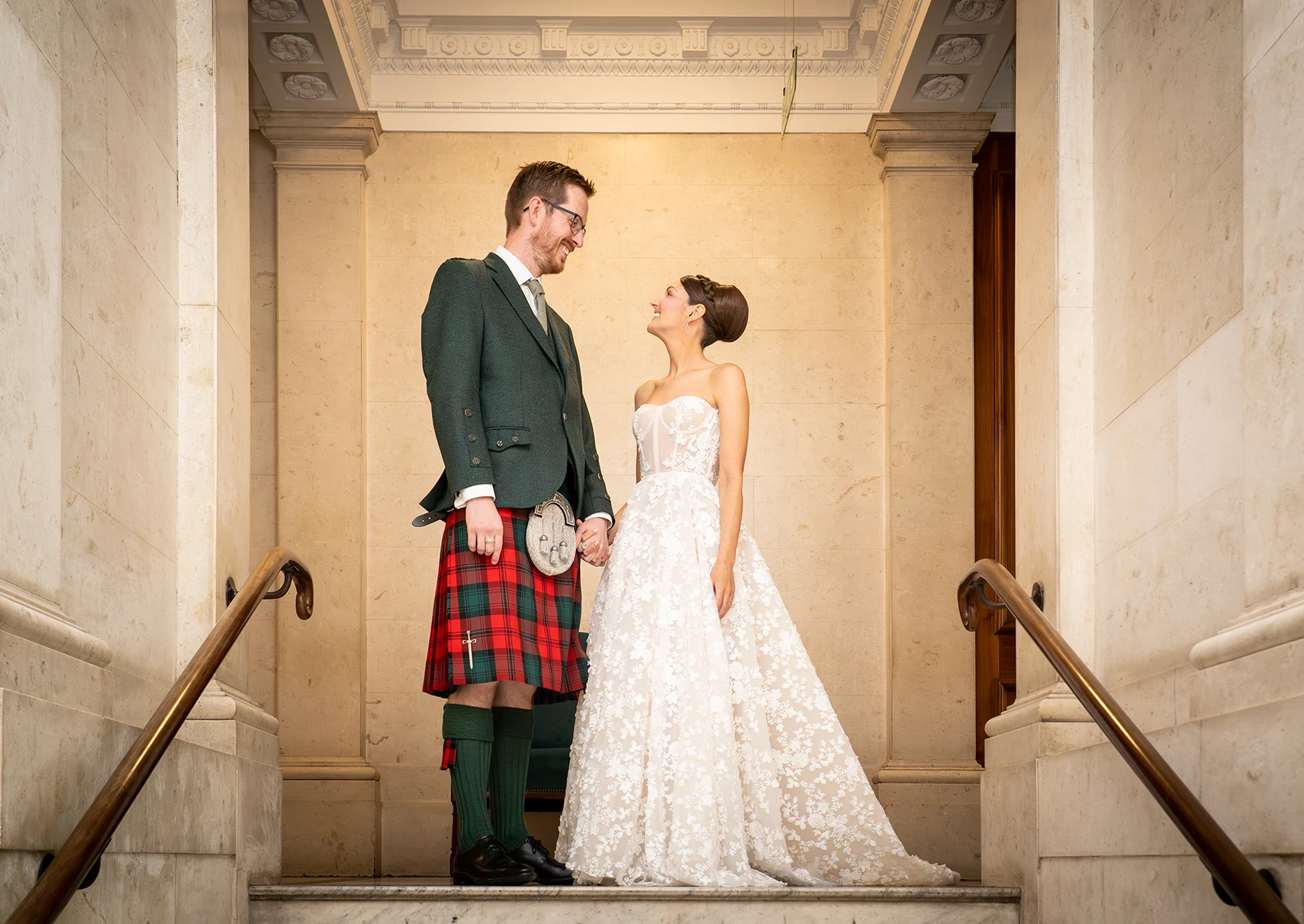 Bride and groom holding hands on marble staircase