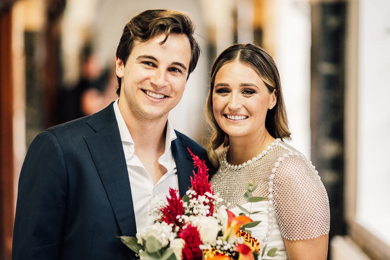 Smiling newlyweds holding bouquet inside historic registry office hallway