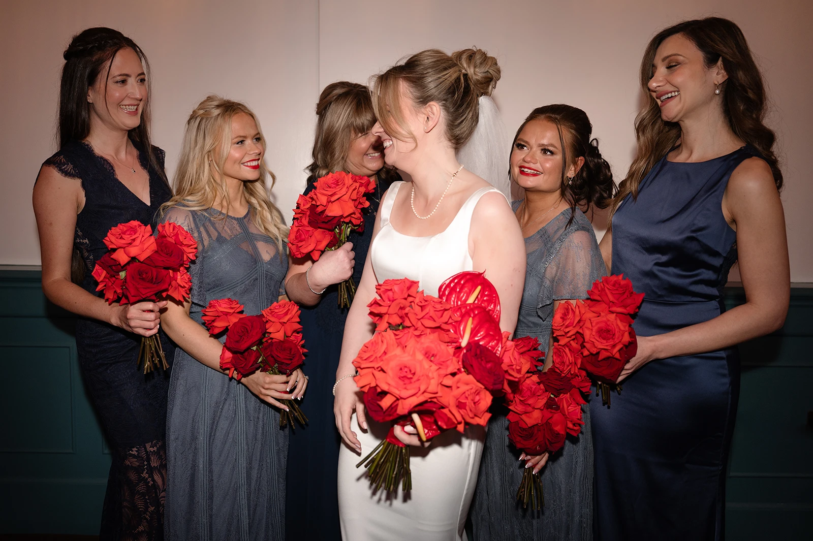 Bride with bridesmaids holding red rose bouquets before wedding ceremony