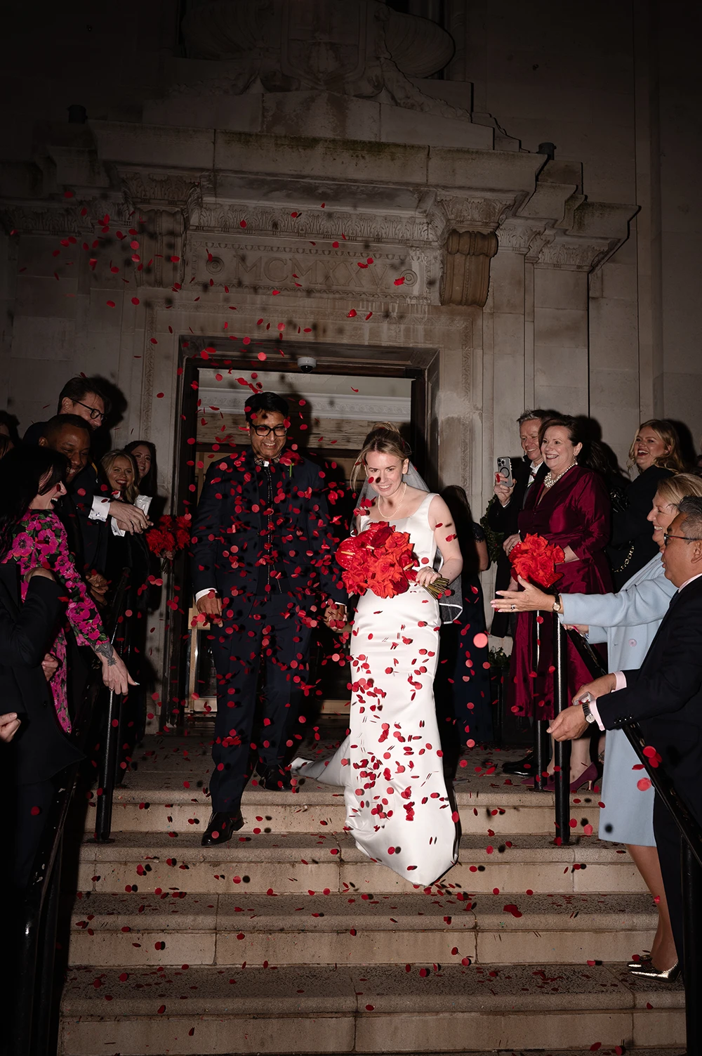 Wedding confetti exit with bride and groom walking down steps as guests cheer